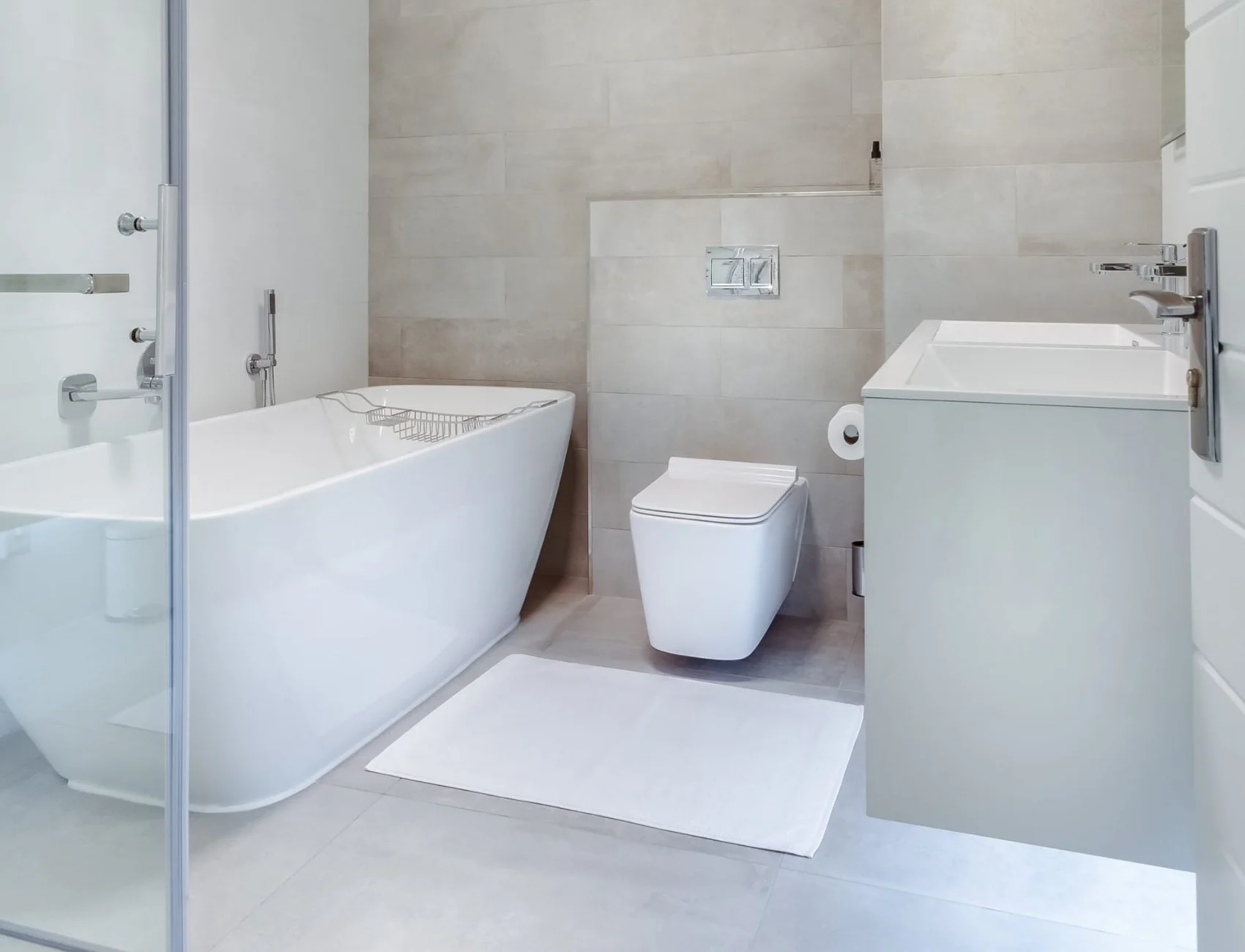 Ein modernes Badezimmer mit minimalistischem Design: Eine freistehende Badewanne, eine schlanke Toilette und ein elegantes Waschbecken stehen vor einer markanten Betonwand, die dem Raum Charakter verleiht.